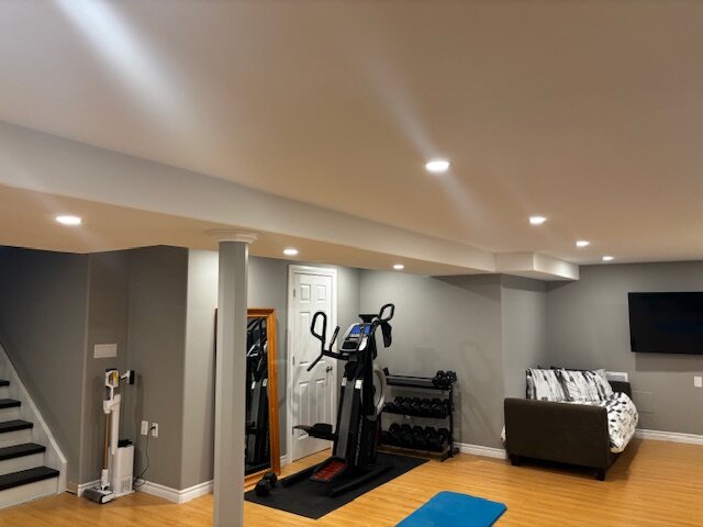 Finished basement with white built-in shelving, grey walls and a home-gym corner